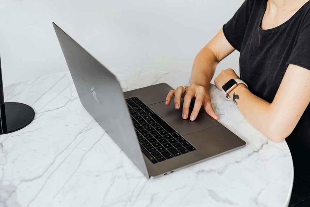 Person using laptop with smartwatch on marble table, showcasing modern technology.